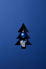 A creative Christmas tree cutout on blue paper, revealing a single glowing ornament and a small gift inside.