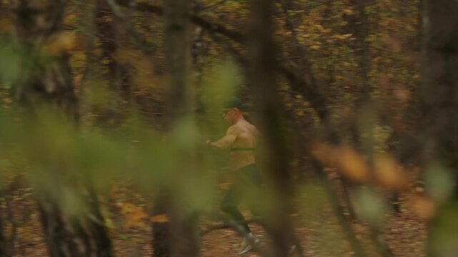 Bodybuilder wearing cap and sunglasses runs along path between trees in an autumn forest with heart rate monitor on his chest.