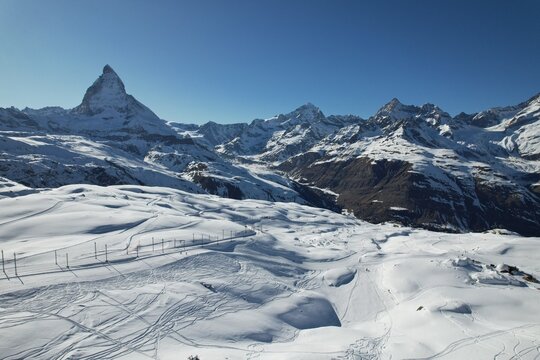 Aerial drone photo of the snowy Swiss Alps near the Matterhorn, showcasing wide glacier fields, winter terrain, and dramatic mountain scenery under a clear blue sky. - Powered by Adobe