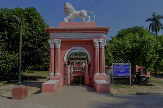 historic pink entrance gate topped with white lion statue leading to the underground 'kathgola bauri – a 18th-century stepped water reservoir and cooling chamber of zamindars, murshidabad