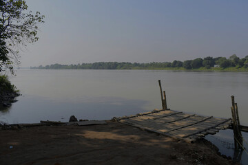 Fototapeta premium a serene fog-covered morning across the bhagirathi river at the traditional ferry ghat of 'sadar ghat', murshidabad, with soft reflections and silent river life