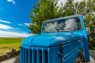 Bright summer midday sun illuminates the vivid blue vintage truck parked by the lush green fields of Southern Iceland