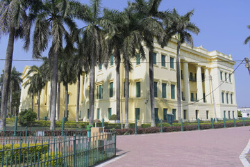 side view of hazarduari palace framed by tall palm trees along the garden pathway in bright daylight