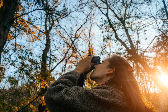 Young Woman Engaging in Photography in Sunny Autumn Forest