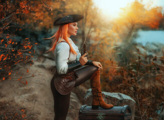 art photograpthy real person beauty woman pirate holds in hands pistol old style gun. trees nature island beach sea, foot is standing on wooden treasure chest. Girl thief. game search for treasure