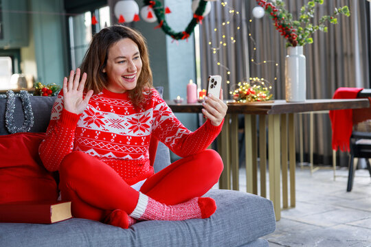 Happy woman in red Christmas sweater waving and winking at phone during holiday video call