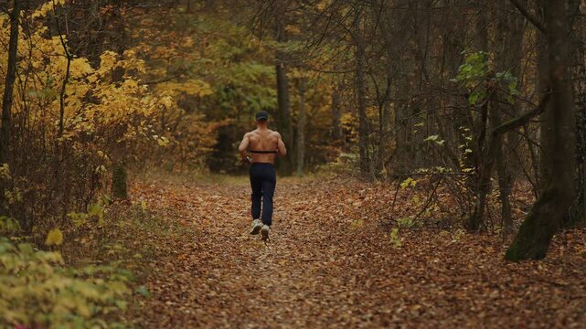 Young muscular shirtless man exercises in an autumn forest