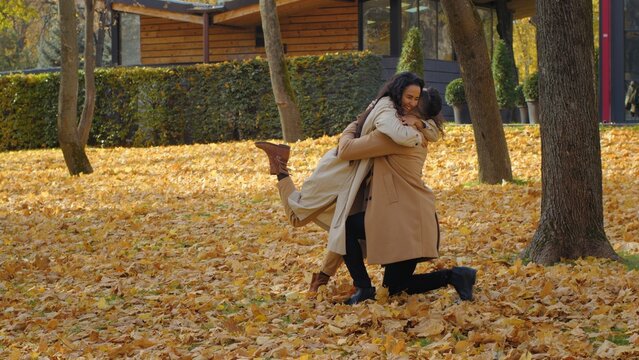 Hispanic loving couple in autumn park man stand on one knee making marriage proposal girlfriend jumping happy say yes affection moment male boyfriend put ring on finger to girl hugging engagement