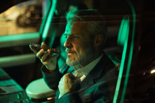 Mature businessman speaking on phone in car at night, focused