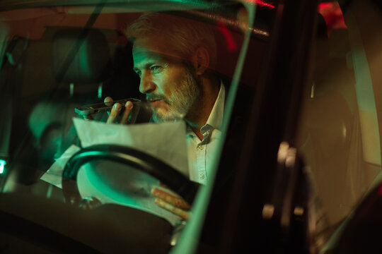 Mature man focused speaking on smartphone in car at night
