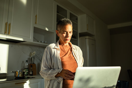 Mature adult focused on laptop in sunlit home kitchen