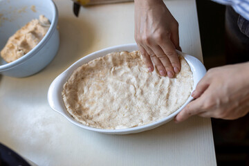 Close-up of hands pressing dough into a white ceramic pie dish on a kitchen counter