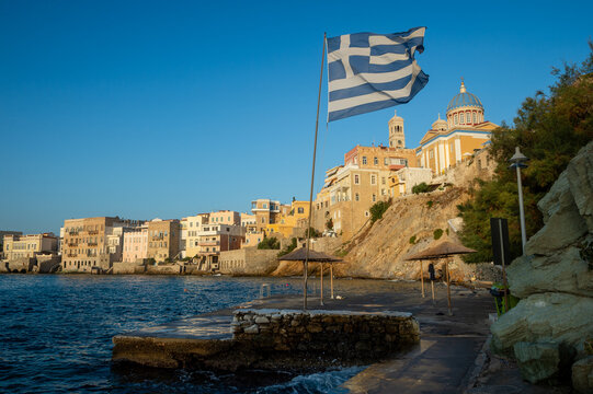 Venetian architecture of Ermoupoli and Saint Nicholas church with a Greek national flag flying from a post in the foreground on a swim platform of Asteria beach on the Greek island of Syros