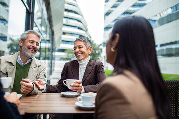 Mature colleagues laughing over coffee at outdoor city cafe