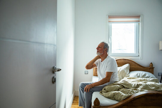 Senior man with neck pain sitting on bed at home