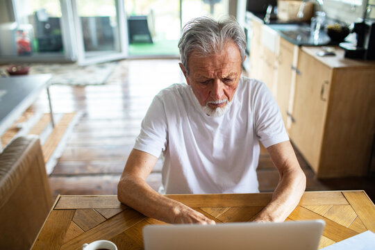 Senior man focused working on laptop at home kitchen table