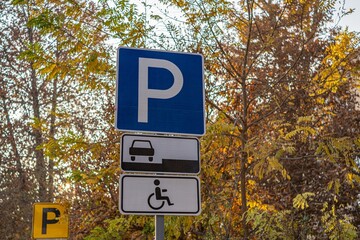 A parking sign indicating spaces for vehicles and accessible parking. Surrounded by autumn foliage, it highlights accessibility features.
