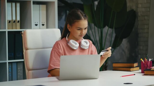 Happy teenage girl shopping online on laptop, entering credit card details