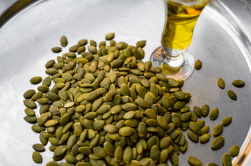 Shelled pumpkin seeds on a plate with a small glass of pumpkin oil –  food composition