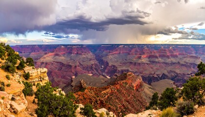 Expansive canyon view under dramatic, stormy skies with colorful rock layers and green shrubbery on the foreground