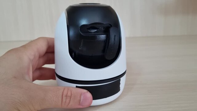 Hand opening the waterproof rubber protective cover on the back of a smart security camera to access the local microSD card storage slot