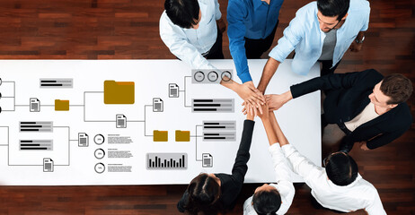 A diverse group of professionals engages in teamwork, showcasing unity and collaboration while discussing strategies over business charts in a modern office environment. Gantry