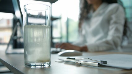 Close-up glass of still water business woman putting pill remedy painkiller inside at office unrecognizable businesswoman female girl worker ill sick manager with computer work preparing vitamin drink