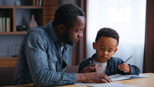 African American family dad assists son with learning teamwork lovely schoolboy with father writing homework at home child kid boy with parent tutor tutoring distant education concentration study - Powered by Adobe