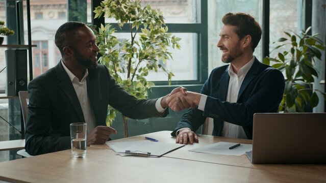 Two happy diverse business men team contract signing shaking hands teamwork cooperation handshaking multiracial businessmen Caucasian man and African American coworkers agreement partnership in office - Powered by Adobe