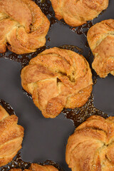 Golden-brown cardamom rolls are baked in a dark pan, sitting in a pool of caramelized syrup and sprinkled with coarse sugar