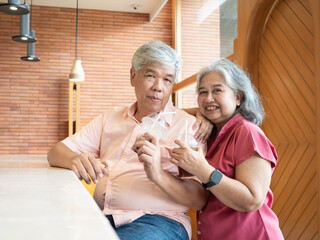 Happy senior Asian couple smiling while drinking iced coffee together at a modern cafe. The elderly man and woman enjoy leisure and quality time, symbolizing a joyful, active retirement.