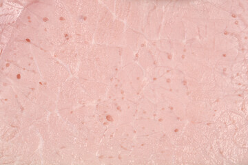 A macro close-up shot captures the smooth, processed texture and pale pink color of a thin slice of deli ham, showing small air pockets within the meat