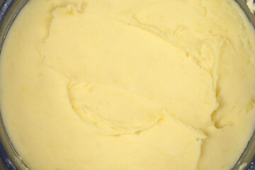 An overhead close-up shot focusing on the smooth, creamy texture and light yellow color of freshly prepared mashed potatoes inside a metal bowl