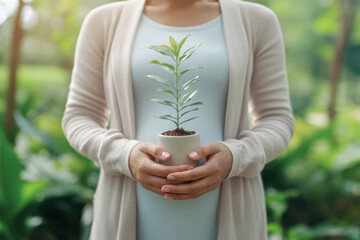 Pregnant woman embracing her growing belly while gently holding a small potted plant, representing motherhood, fertility, and the nurturing of new life in a lush green outdoor setting