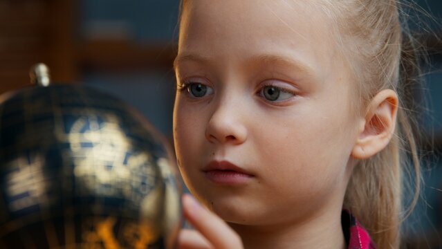 Close up little Caucasian child kid girl daughter rotating gold globe studying at evening home baby exploring world search countries dreaming traveling study geography planet cartography navigation