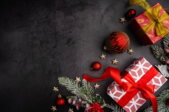 Christmas gift boxes with red and gold ribbons, Christmas ornaments, frosted pine branches, and red flowers on dark background. Ideal for holiday cards, festive ads, and winter promotions. - Powered by Adobe