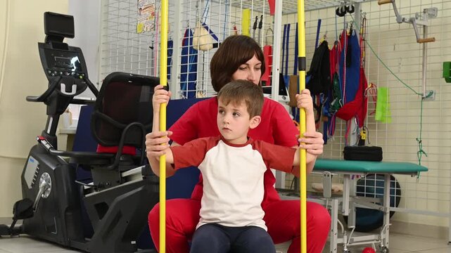 A physical therapist works with a child on posture exercises. A professional osteopath helps a boy do scoliosis exercises with gymnastic sticks.