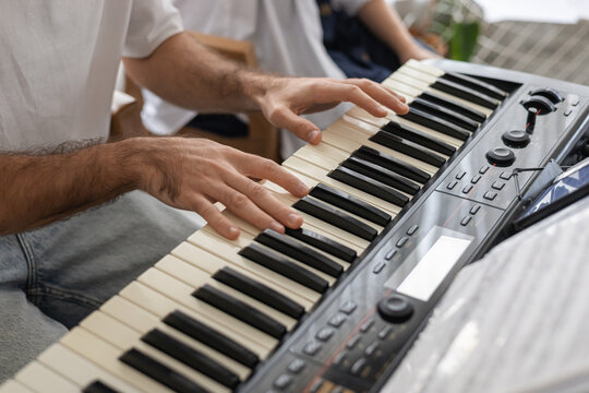 A close-up of a mans hands playing a keyboard in a cozy home setting. The atmosphere is relaxed and inviting, perfect for family music sessions.