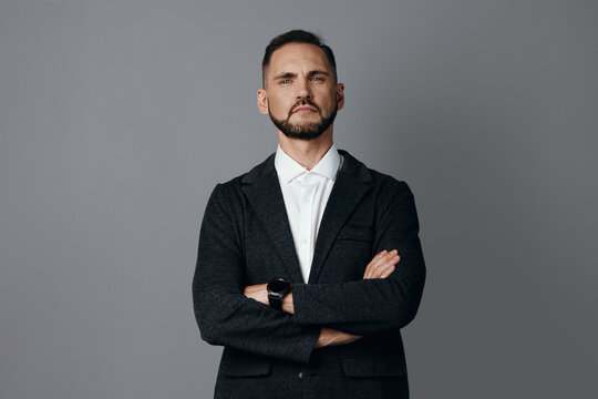 A professional male business figure stands with arms crossed against a solid colored background, projecting confidence, focus, determination, and poised authority in a corporate setting.