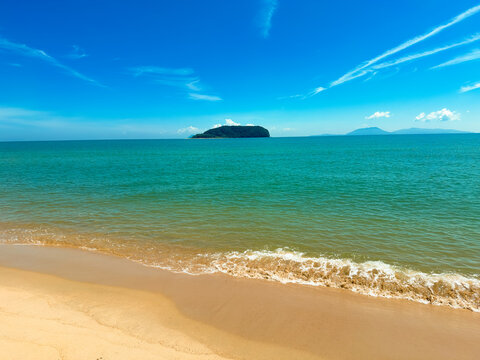 A clear sunny view of Pantai Bukit Keluang with turquoise waters, gentle waves, and an island visible on the horizon.
