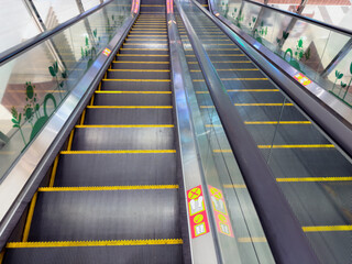 Escalator in a shopping mall featuring safety markings and yellow step edges, viewed from above.