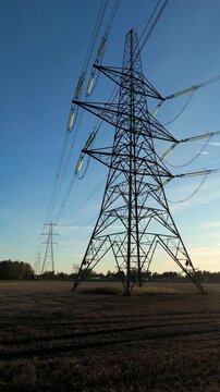 Aerial view of tall electricity pylons contrasting against the clear blue sky and harvested field, Cambridge, England, United Kingdom.