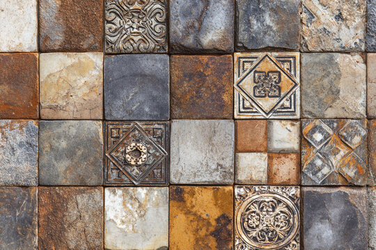 A textured wall of various stone tiles some with decorative embossed patterns in earthen tones