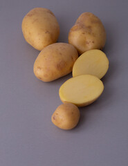 Macro view of whole and half-cut fresh potatoes, highlighting natural skin marks, yellow inner flesh, and organic texture on a minimal neutral surface.