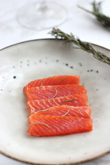 Trout slices lie in a plate on a marble table, with rosemary nearby.