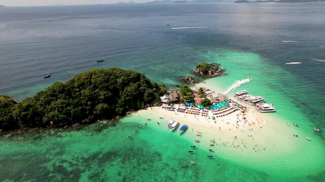 An aerial drone view of Koh Khai Nok in Thailand, showing turquoise water, crowded sandy beaches, colorful umbrellas, and speedboats anchored along the shore