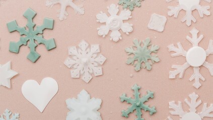 Close up of various pastel colored snowflake and heart shaped decorations scattered on a textured light peach background