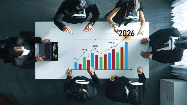 A group of professionals engages in a business meeting utilizing virtual reality technology to analyze financial trends and forecasts for future growth from 2023 to 2026. Trope