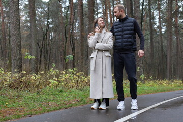 Fototapeta premium Couple enjoying an autumn walk in the forest, woman on a phone call