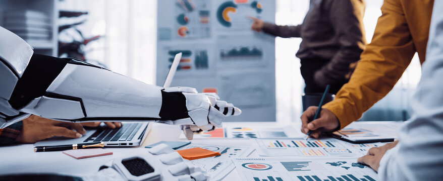 A futuristic workspace showcasing a robot hand assisting in collaborative data analysis. Professionals engage with charts and technology, highlighting modern teamwork dynamics.Noogenesis - Powered by Adobe